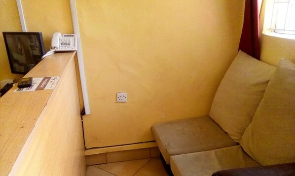 A compact room with a wooden desk, a cushioned bench, and a power outlet on the wall.