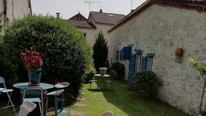 Een verzorgde tuin met gazon, een rieten schommelstoel, een ronde tafel met stoelen en een potplant.