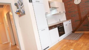 Une cuisine de taille réduite avec des meubles blancs, un four encastré et une horloge au mur.