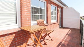 Une terrasse avec une table et des chaises en bois, un mur en briques et de grandes fenêtres.