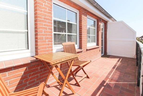 A patio with a wooden table and chairs, a brick wall, and large windows.