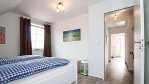 Une chambre à coucher avec un lit, une table de chevet, un tableau et une vue sur un couloir.