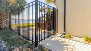 A gated area with a metal fence, a concrete pathway, and a body of water in the background. - Waterview penthouse condo on inter coastal waterway with pool (Fort Walton Beach)