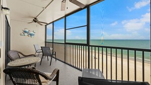 Un balcón con mobiliario de mimbre, ventilador de techo y vista a la playa.