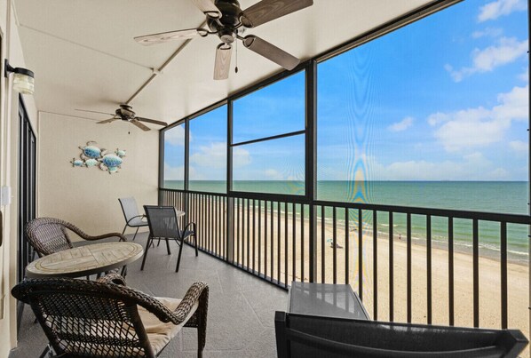 A balcony with wicker furniture, a ceiling fan, and a view of the beach.