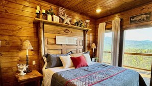 A wooden cabin bedroom with a large bed, wooden walls, a nightstand with a lamp, and a sign reading "Hibernation Station". - MORE THAN A GORGEOUS CABIN, IT'S AN EXPERIENCE!!!!  CLOSE TO ATTRACTIONS & GSM (Sevierville)