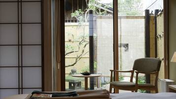 A traditional Japanese-style room with tatami flooring, a low table with a tea set, a chair, and a bed with neatly folded towels.