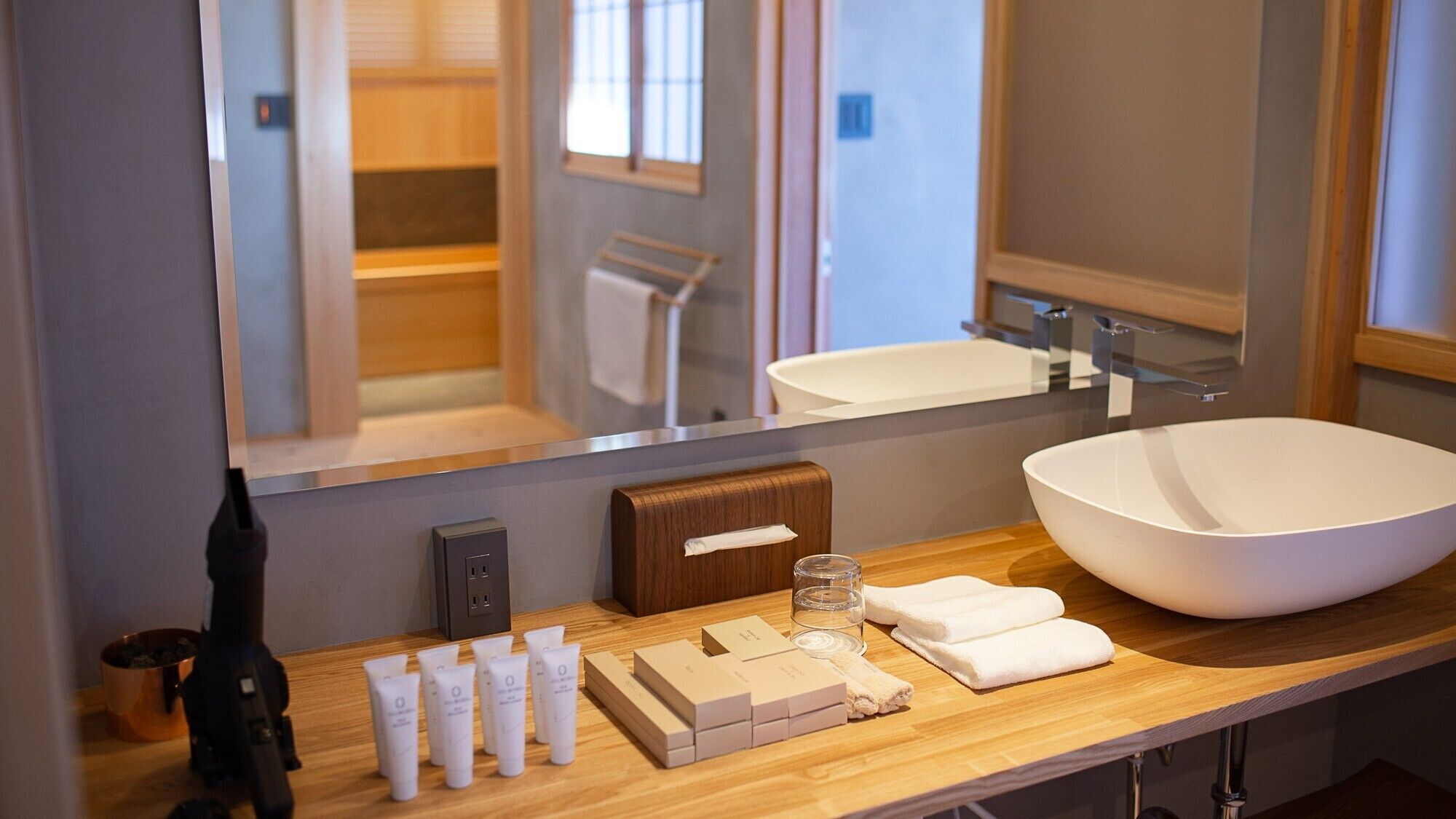 A modern bathroom with a large white sink, wooden vanity, and a mirror reflecting a shower area.