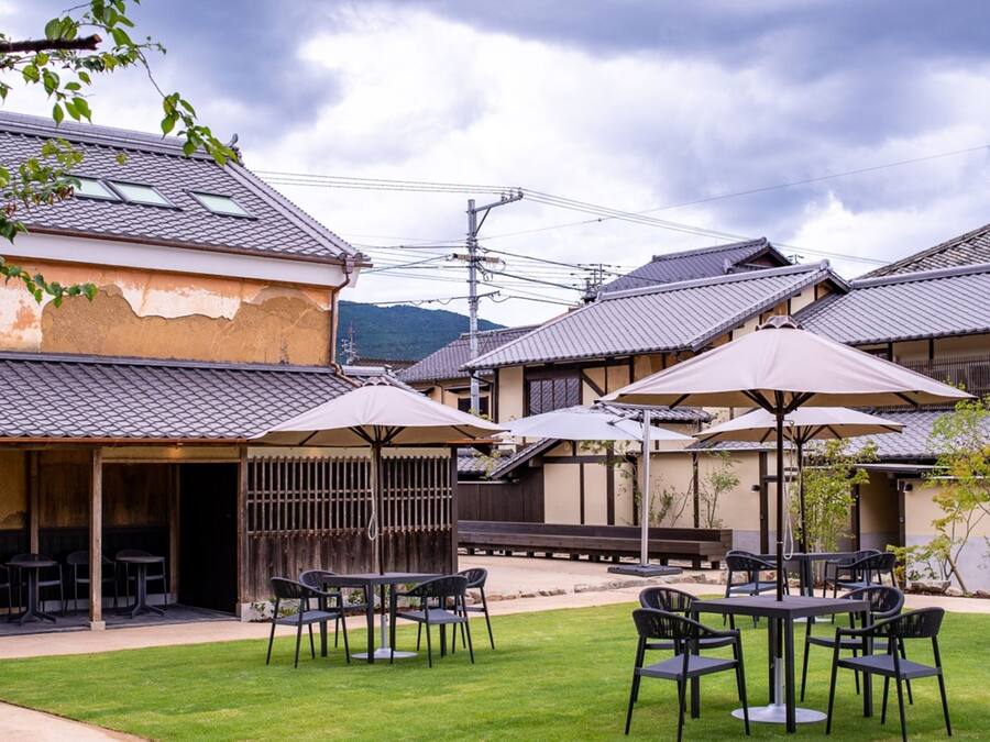 An outdoor seating area with tables and chairs, umbrellas, and a building with a tiled roof.