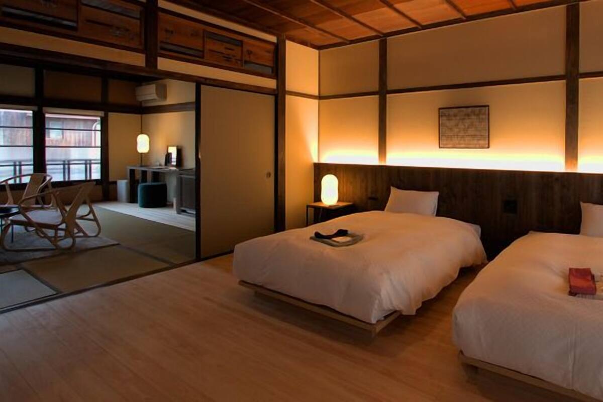 Habitación de hotel con dos camas, suelo de madera, un escritorio con silla y vista a través de una ventana.