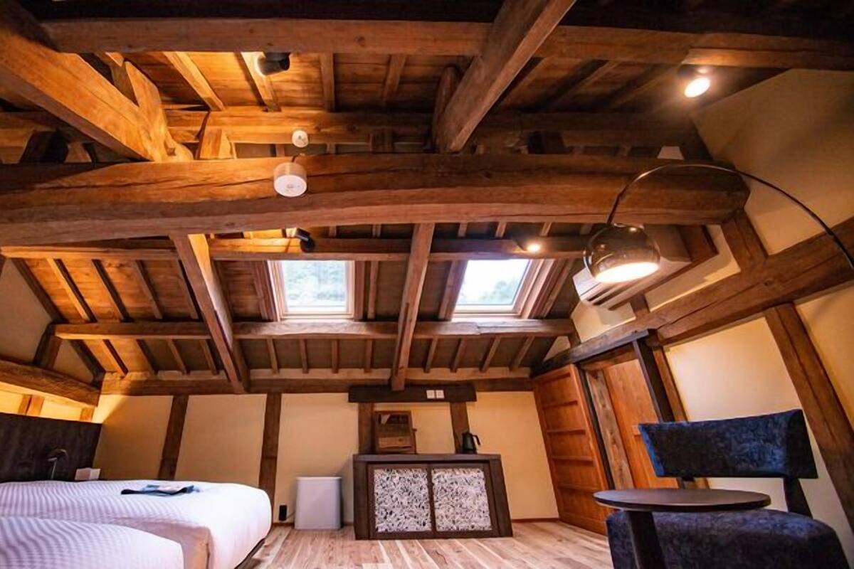 Una habitación rústica de madera con una cama, un escritorio y una silla. Hay dos tragaluces que dejan entrar luz natural.
