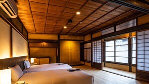 Una habitación tradicional japonesa con suelo de tatami, una cama grande, puertas correderas y un ventilador de techo.