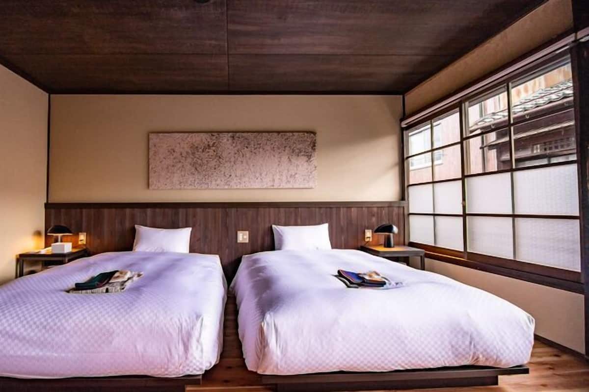 Habitación doble con dos camas, cabeceros de madera, un ventanal grande con persianas y una obra de arte colgada en la pared.