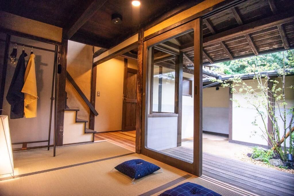 A traditional Japanese room with tatami flooring, a sliding door leading to an outdoor area, and a view of greenery outside.