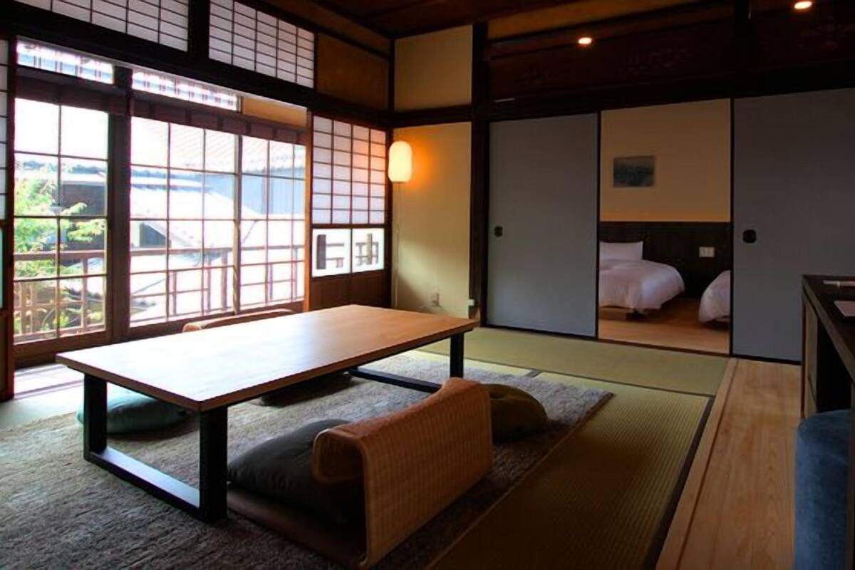 Una habitación japonesa tradicional con suelo de tatami, una mesa baja y puertas correderas que dan a un dormitorio.