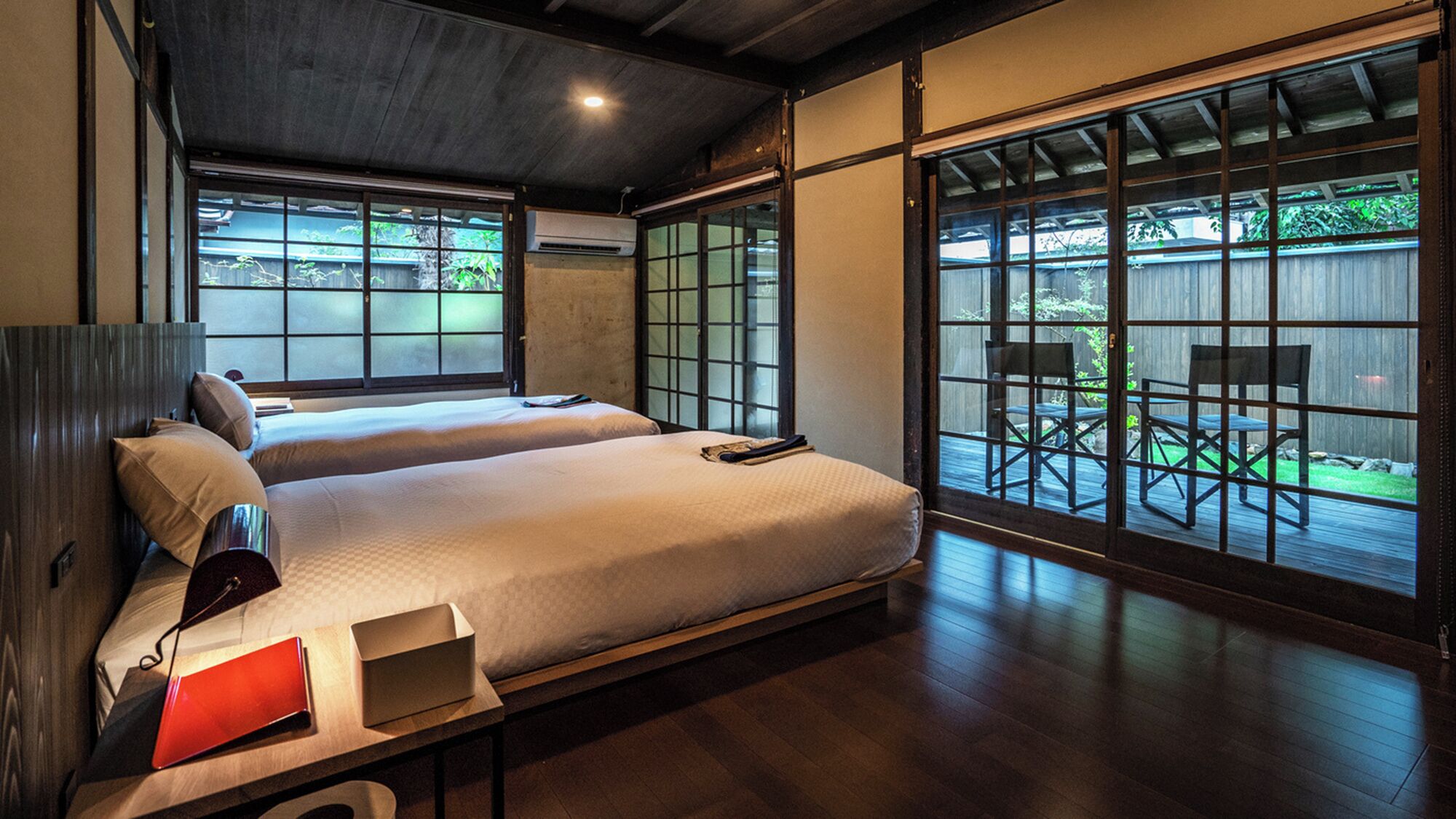 A hotel room with a large bed, a desk, and a view through a sliding door to an outdoor deck.