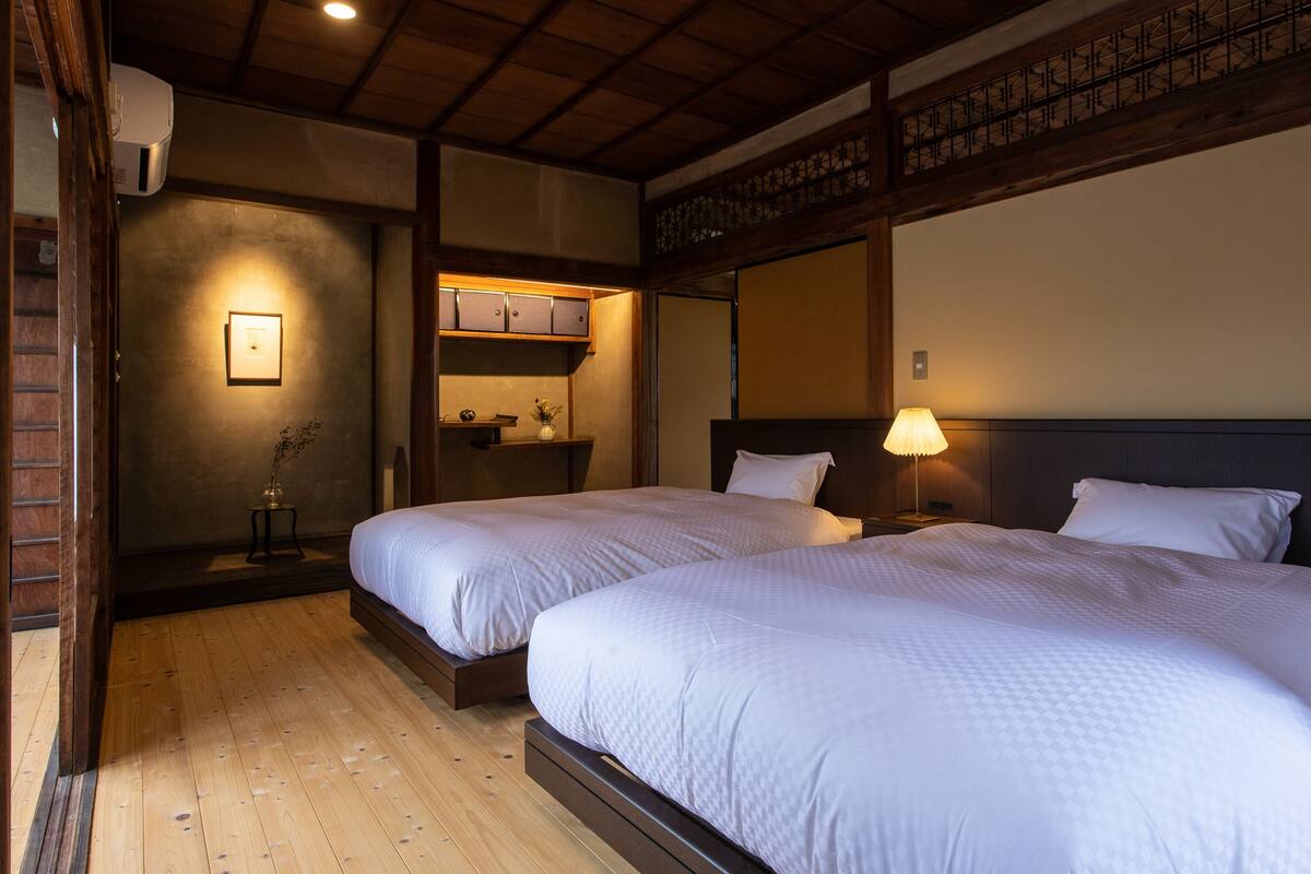 Habitación de hotel con dos camas, suelo de madera, estante empotrado con espacio de almacenamiento, aire acondicionado de pared y un cuadro enmarcado.
