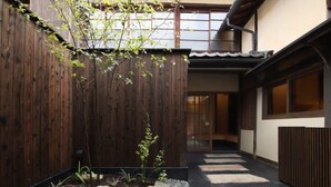 Un patio tradicional japonés con valla de madera, un camino de grava y un pequeño jardín con rocas y plantas.