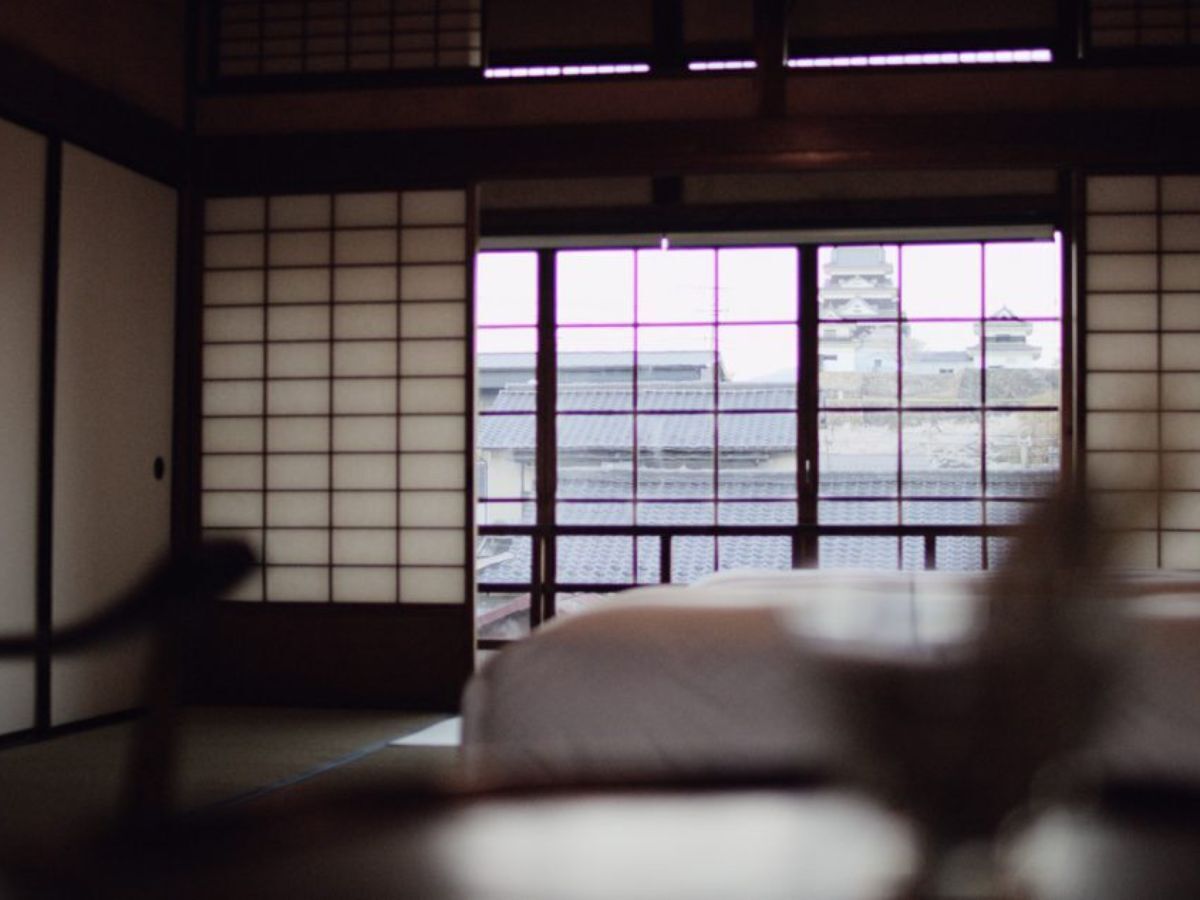 A traditional Japanese room with tatami flooring, a low table, and a view of a building through a shoji screen.