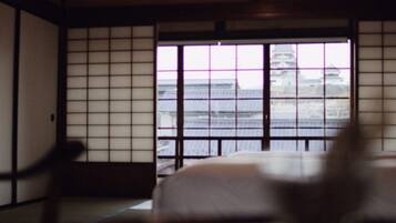 A traditional Japanese room with tatami flooring, a low table, and a view of a building through a shoji screen.