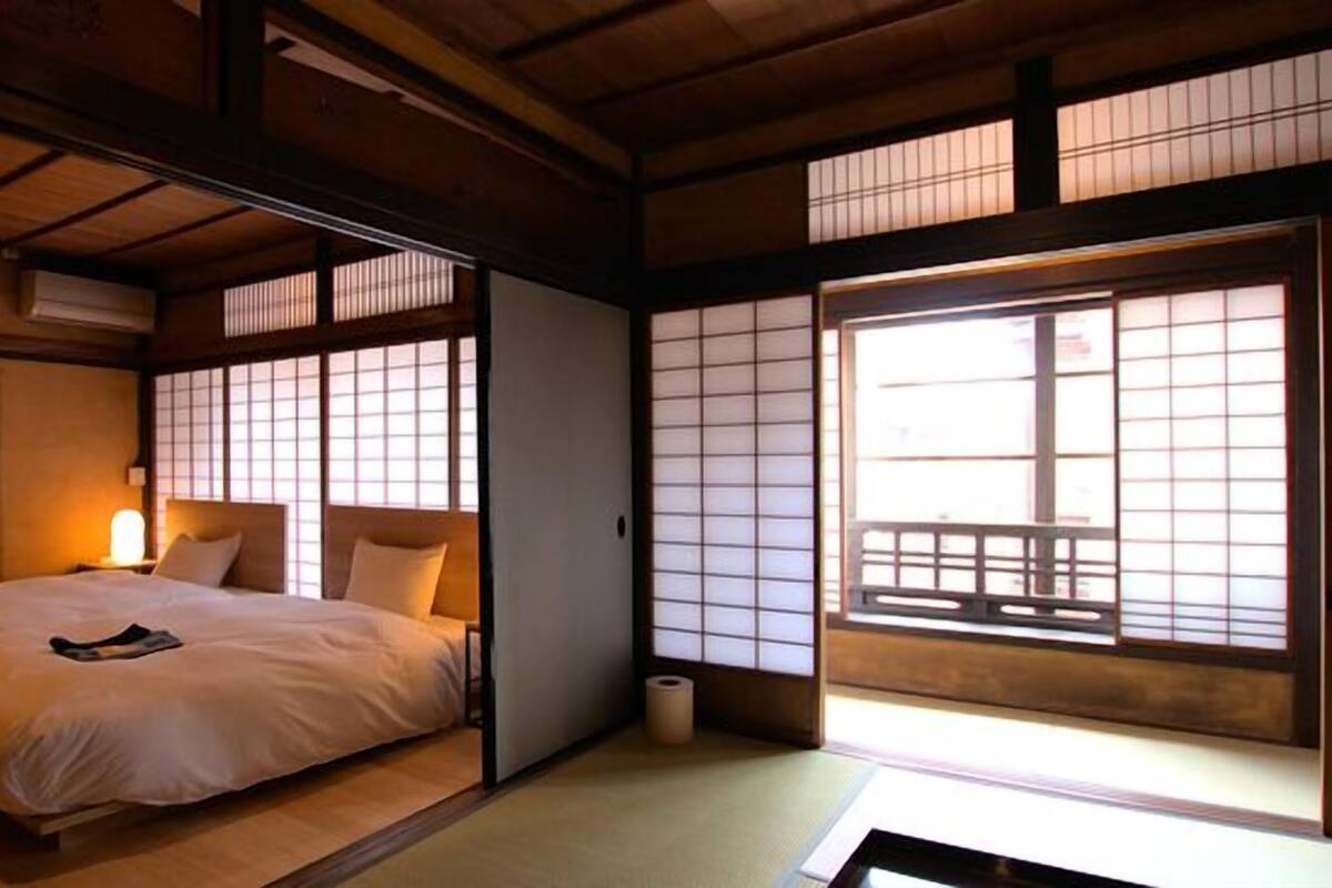 Una habitación tradicional japonesa con suelo de tatami, una cama baja con futón, puertas correderas shoji y vistas a un balcón.