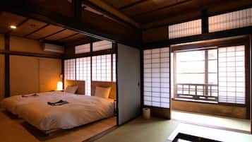 A traditional Japanese-style room with tatami flooring, a low bed with a futon, sliding shoji doors, and a view of a balcony.