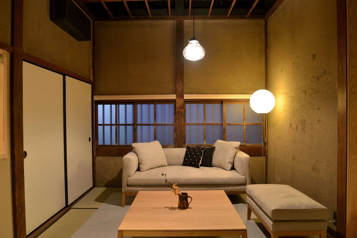A traditional Japanese room with tatami flooring, a low wooden table, a sofa with cushions, and a sliding door.