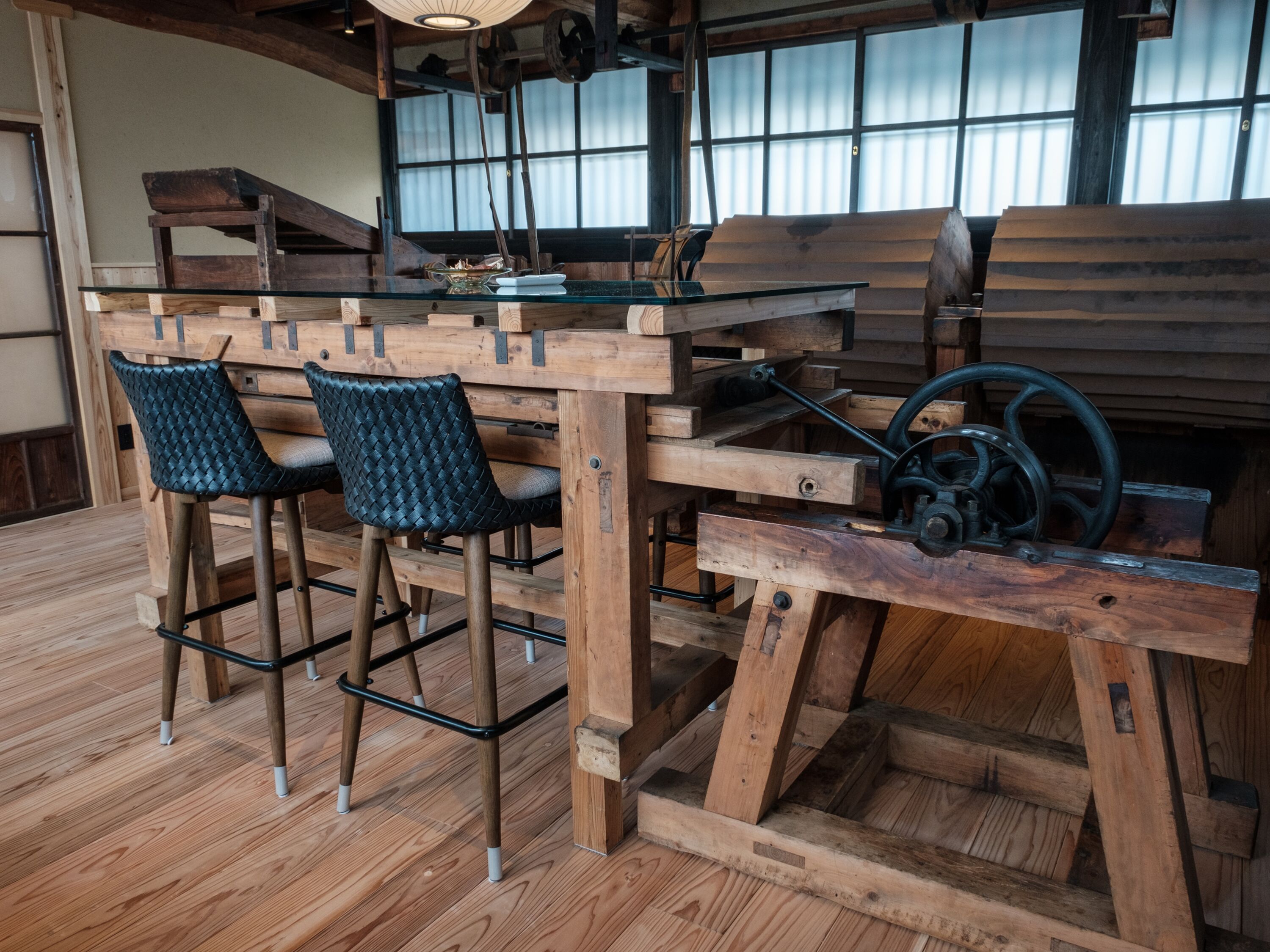 A rustic wooden bar area with a large wooden table, two woven chairs, and a vintage mechanical device.