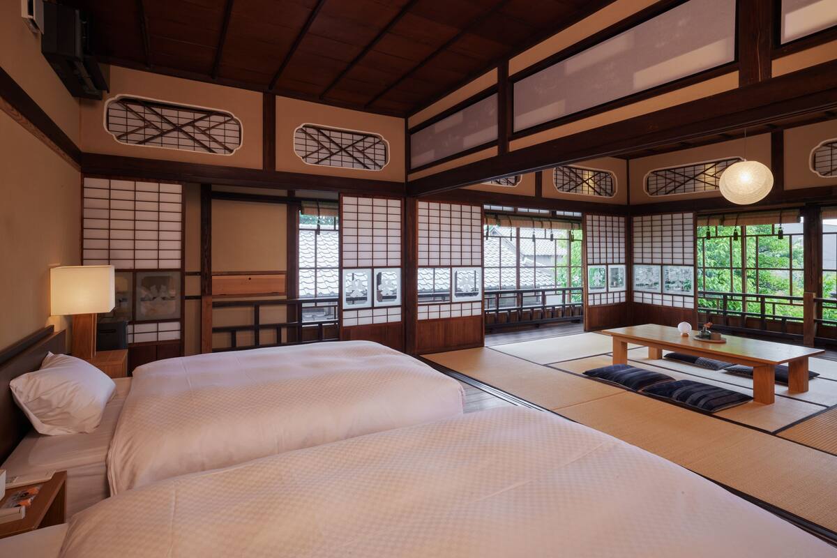 A traditional Japanese-style room with tatami flooring, a low wooden table, and a bed with white bedding.