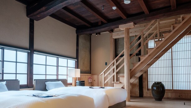 Habitación de hotel con una cama grande, un escritorio, una lámpara, un ventanal amplio y una escalera.