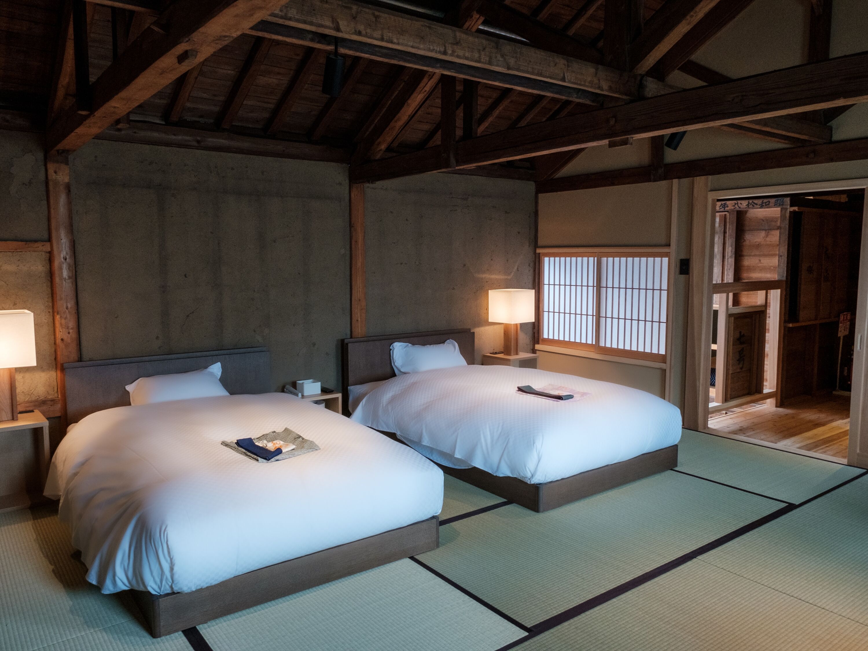 Een traditionele Japanse kamer met twee bedden, tatami vloeren en houten balken in het plafond.