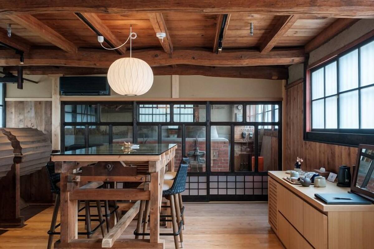 A rustic kitchen with wooden beams, a large window, and a hanging light fixture.