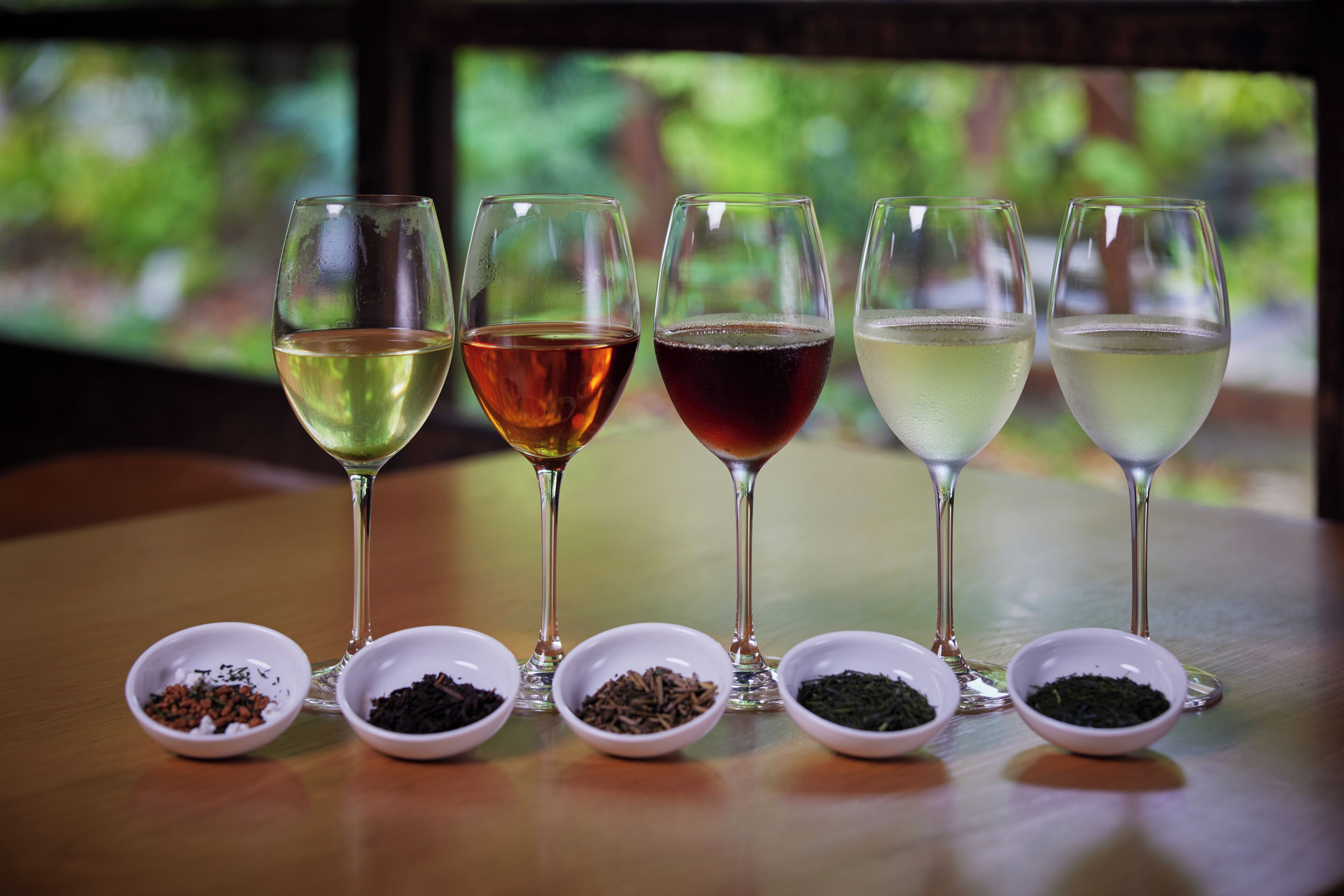 Seis copas de vino con líquidos de colores distintos y cuatro recipientes pequeños con diversas especias o hierbas.