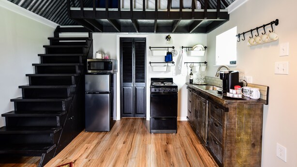 A compact kitchen with a wooden staircase, a microwave, a refrigerator, a stove, and a coffee maker. - Queens Hotel- a cozy studio cottage in the country. Pool and hot tub.  (Round Top)