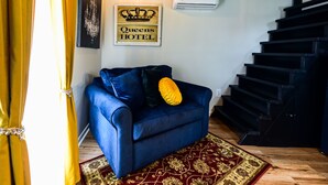 A blue sofa with a yellow pillow, a red patterned rug, a staircase, and a sign that reads "Queens Hotel". - Queens Hotel- a cozy studio cottage in the country. Pool and hot tub.  (Round Top)