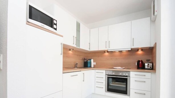 A modern kitchen with white cabinets, a built-in microwave, a stove, and a toaster. - Kerstins Mühlenplatz (Krummhoern)