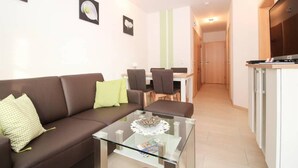 A modern living room with a brown sofa, a glass coffee table, and a dining area with chairs and a table. - Kerstins Mühlenplatz (Krummhoern)
