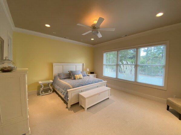 Une chambre à coucher comprenant un lit, une table de chevet, un banc, un ventilateur de plafond et une fenêtre avec des stores.