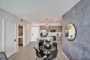 A modern kitchen with a central island, a dining area with a round table, and a large mirror on the wall.
