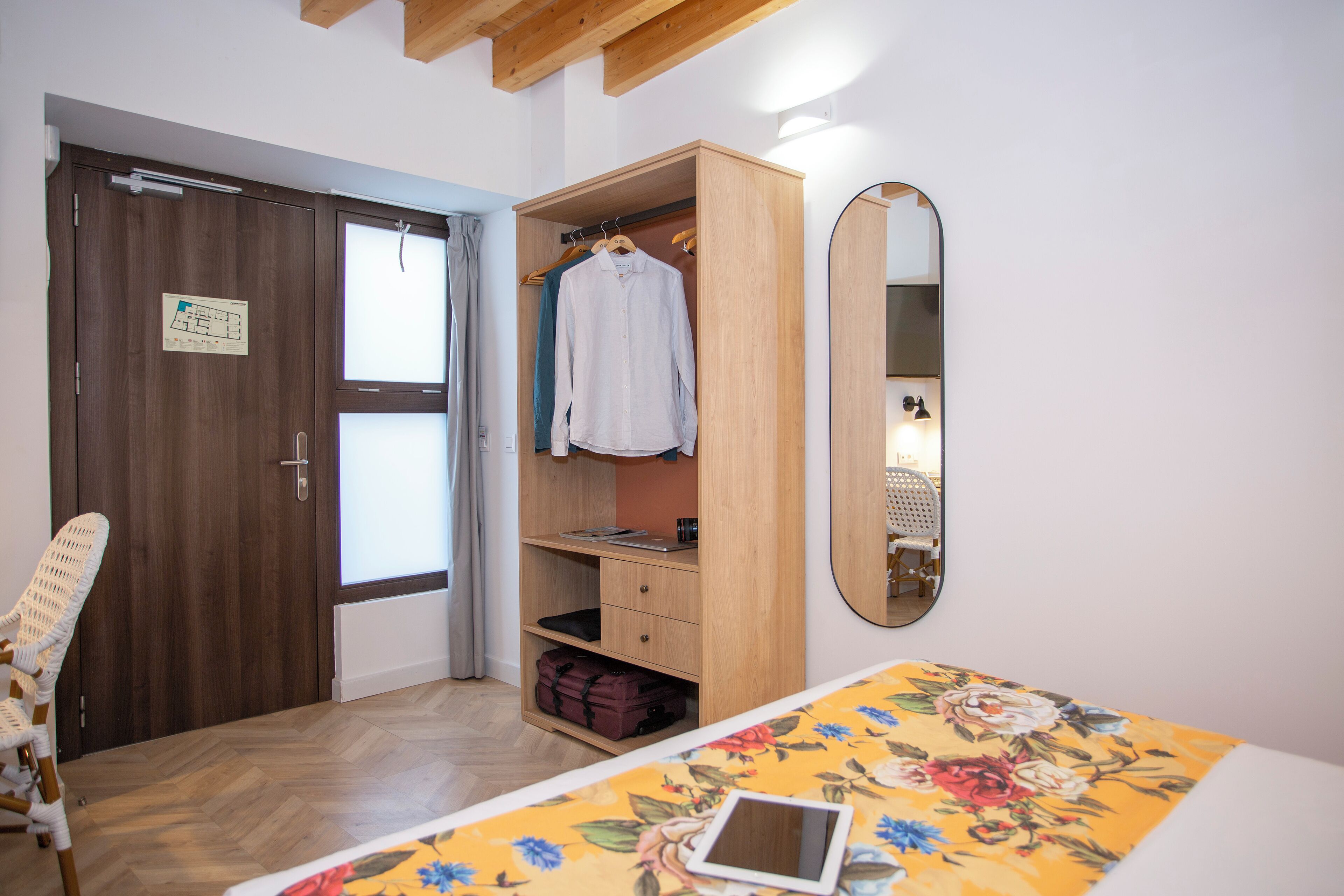 Un dormitorio con un armario de madera, una cama con colcha estampada, una silla blanca y un espejo en la pared.
