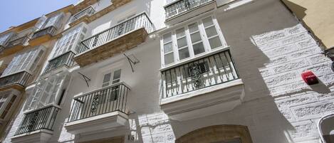 Un edificio de varios pisos con fachadas blancas, varios balcones con barandillas negras y un detector de incendios visible.