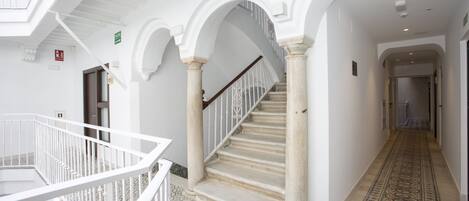 Un pasillo amplio con una imponente escalera, columnas blancas y pavimento con diseños.