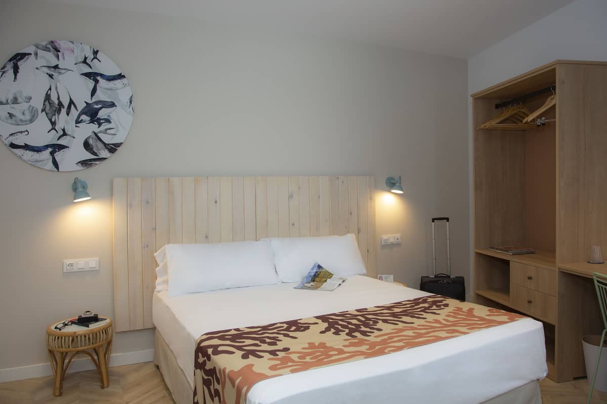 Een netjes ingerichte hotelkamer met een bed, nachtkastje, wandlamp en een kledingkast.