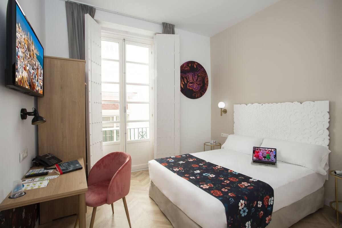 Een hotelkamer met een bed, een bureau, een stoel, een televisie en een deur naar een balkon.
