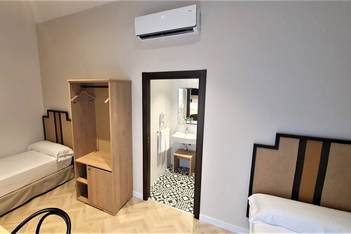 Een kleine hotelkamer met een enkel bed, een kledingkast, een tafeltje en een badkamer die door een geopende deur zichtbaar is.