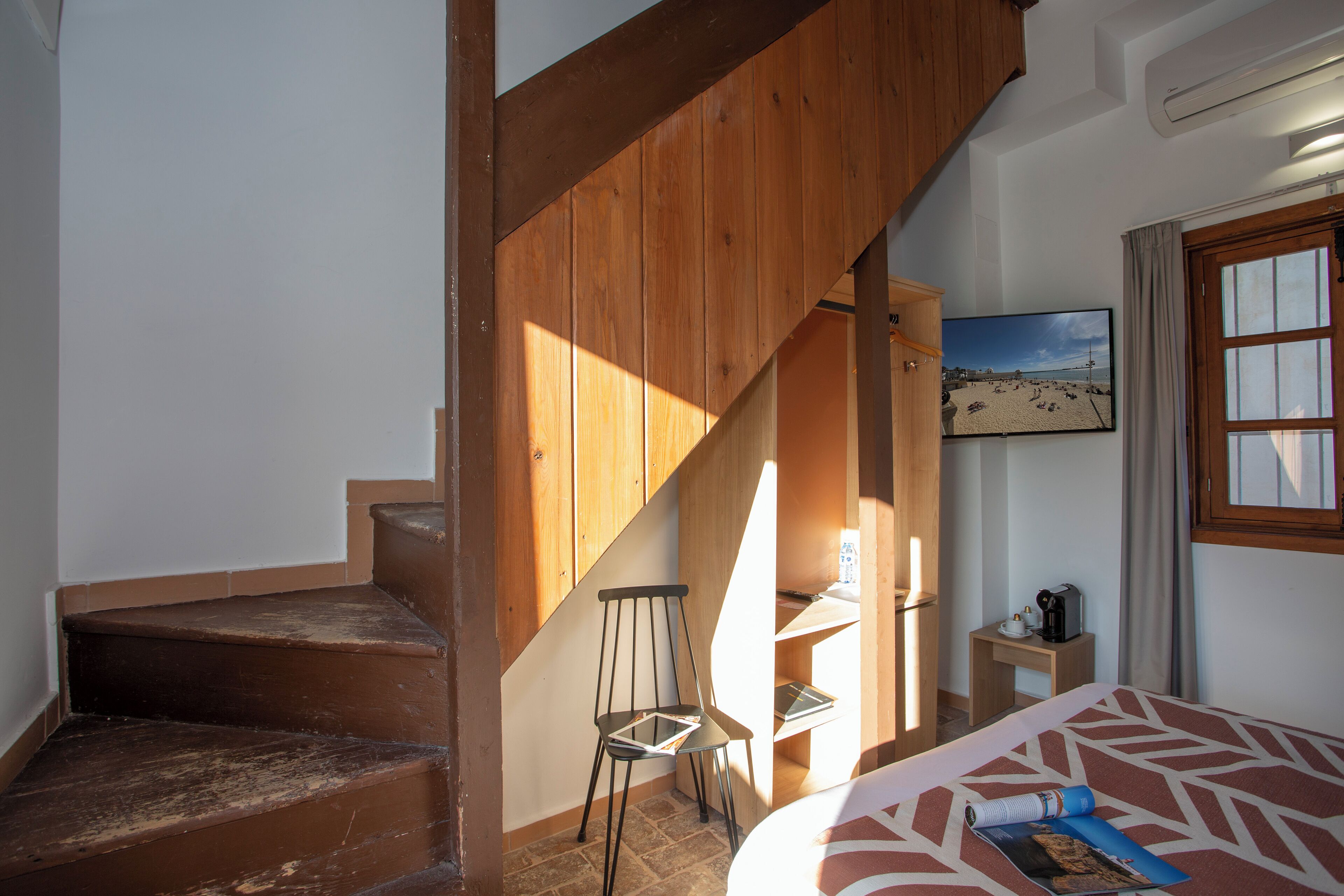 Un dormitorio con una cama, una silla, una mesita, un cuadro en la pared y una escalera.