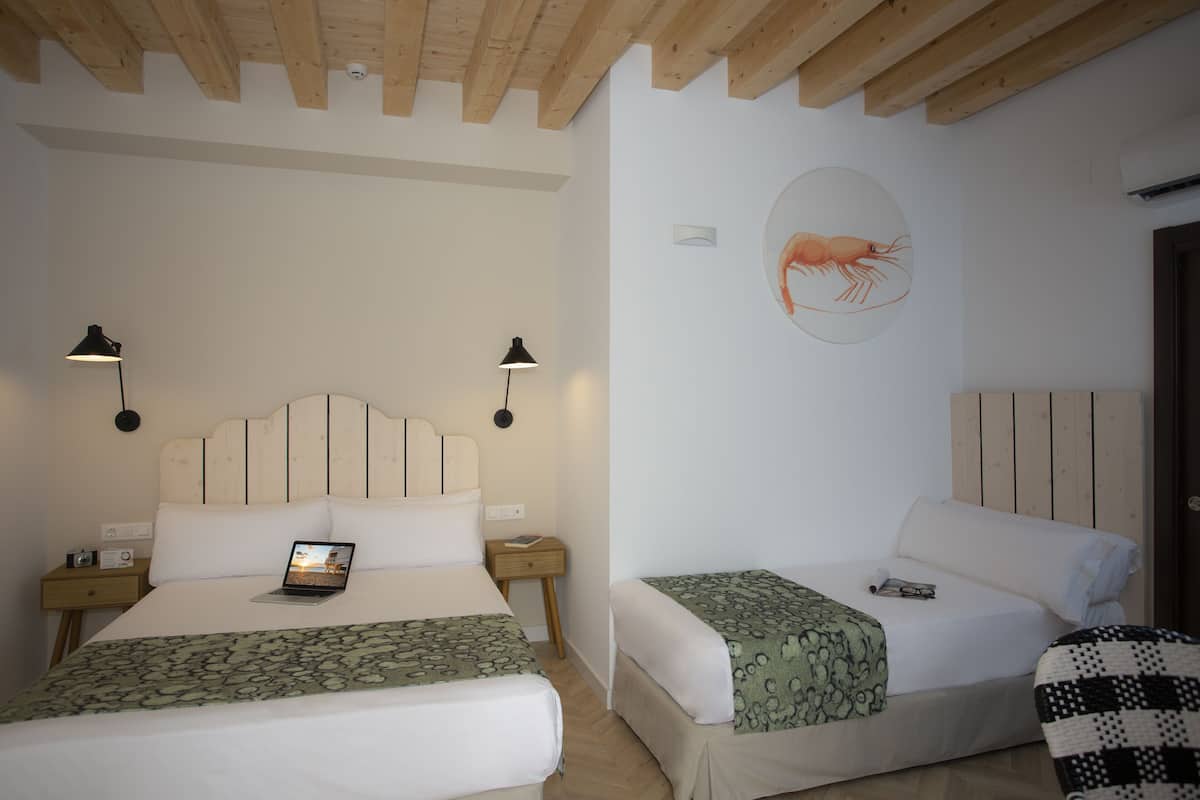 Een slaapkamer met twee bedden, een laptop op een van de bedden en een aan de muur hangend kunstwerk van een garnalen.