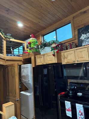 Una cocina con armarios de madera, un refrigerador negro, un microondas y una ventana sobre el fregadero.