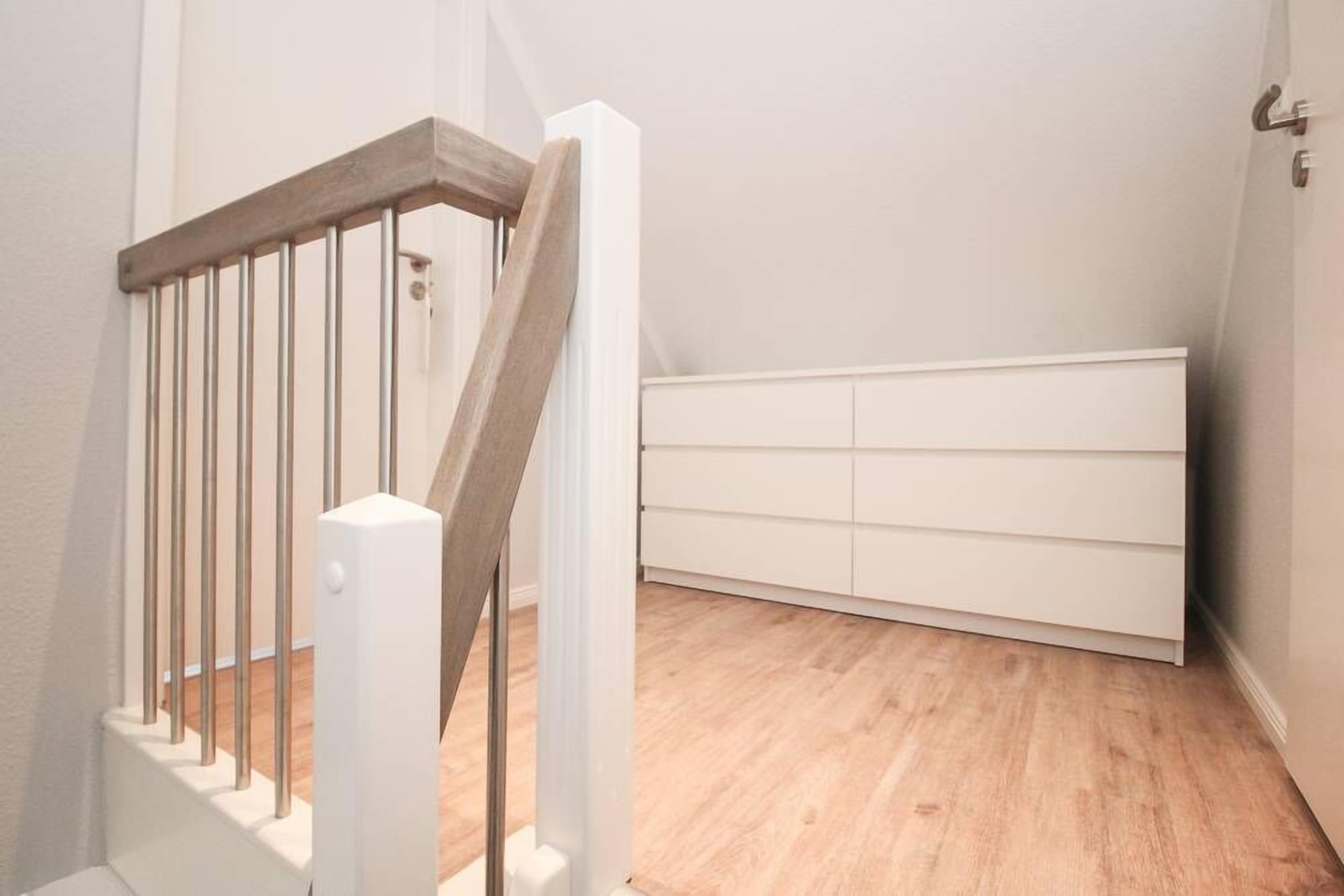 A staircase with wooden handrails and a white wall with a built-in white cabinet.