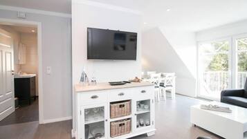 Uma sala de estar moderna com um rack branco, uma TV de tela plana e um espaço de jantar com mesa e cadeiras brancas.